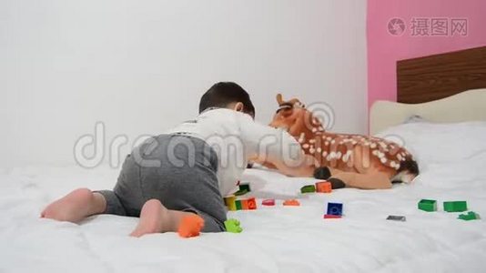 一个半岁的男孩在床上玩乐高积木和软玩具视频