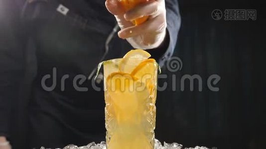 特写厨师将橙子以慢动作挤压到新鲜水果鸡尾酒上。果汁从水果里滴出来。烹调视频