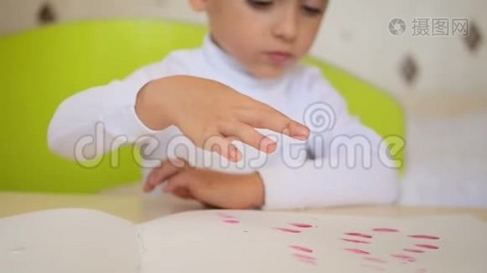 快乐的孩子坐在桌子旁用水彩作画。 小男孩把手指放在颜料里涂抹视频