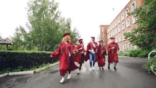 多莉拍摄了兴奋的毕业生穿着长袍和传统帽子在校园里奔跑，庆祝学业结束。 高等视频