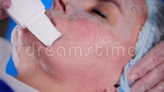 美容诊所。年轻女性由按摩师用面霜和工具在面膜中进行专业的面部按摩。视频