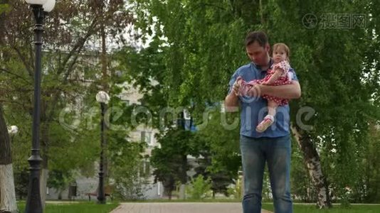 可爱的爸爸把她的女儿穿在夏天的绿色公园里的凉鞋上。视频