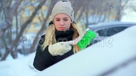 一个年轻的女孩用她的车刷从雪中清洁绿色。 冬天的早晨视频