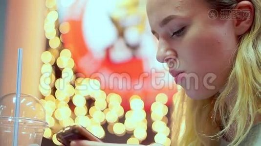 年轻的少女读智能手机信息。 她正在咖啡馆里吃晚饭。 快餐，晚上，在灯光的背景下视频