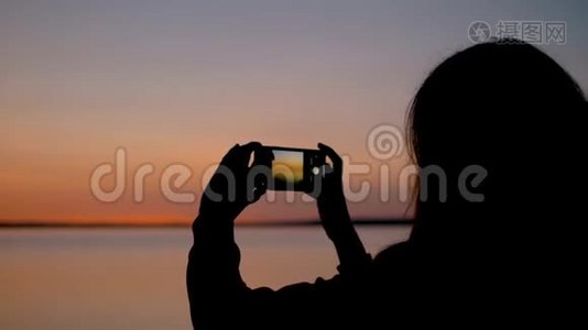 一个女人在智能手机上拍照海上日落视频