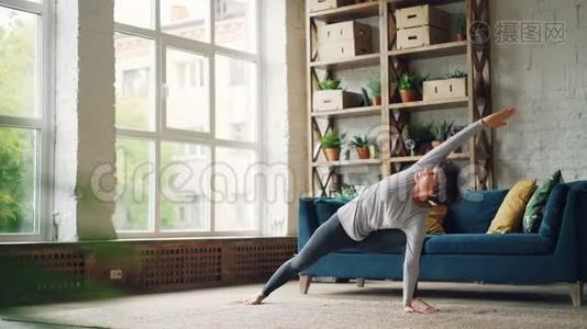 灵活的年轻女性在家锻炼，在现代公寓的地板上练习瑜伽体式，伸展身体、手臂和身体视频