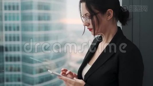 商业女性的特写肖像，手里拿着一部智能手机。 一个穿着商务服的女人站在一个大个子旁边视频