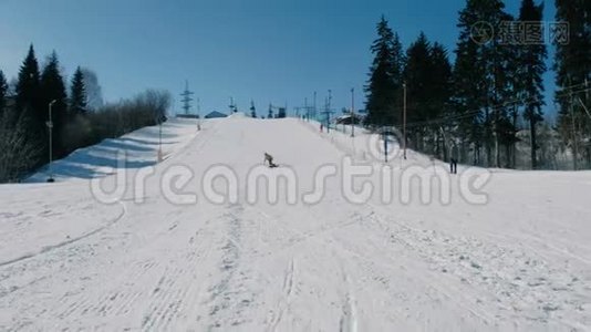 穿黄色夹克的人在电梯旁边的一个滑雪板斜坡上下山。视频