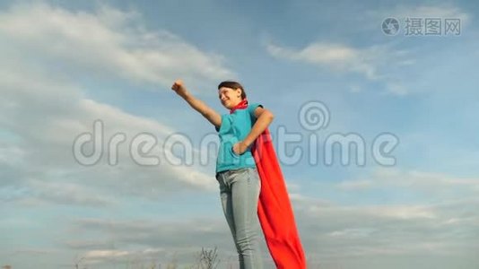 美丽的女孩超级英雄穿着红色斗篷站在田野上，斗篷随风飘扬。 慢动作。 特写镜头。 女孩的梦想视频