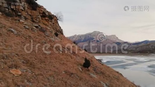 以史诗般的岩石和悬崖为背景，在冻结的山湖畔鸟瞰山坡和悬崖。视频