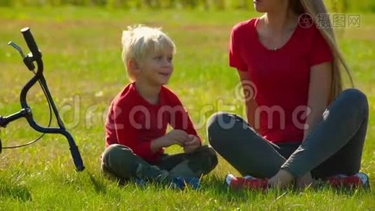 一个年轻的女人和她的小儿子坐在草坪上，旁边放着一辆自行车视频