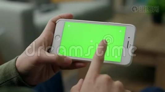 一个男人在智能手机上选择一个角色，客厅里有一个绿色的屏幕视频