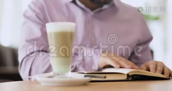 一个人正在看一本书，他的手指在书页上，坐在咖啡馆里，前面是一杯卡布奇诺。视频
