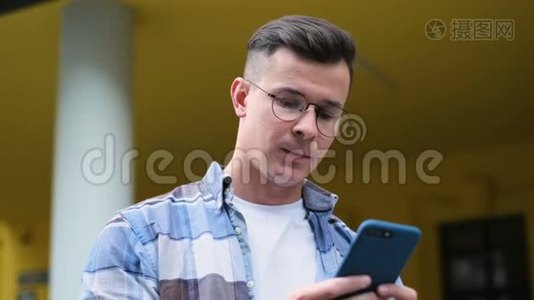 一位英俊的年轻人用智能手机在社交媒体上滚动，以设备、笑声和视频