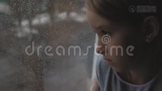 伤心的少年女孩在雨天透过窗户看着外面。视频