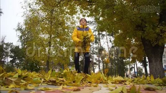 快乐的女孩在秋天在公园里扔黄叶，微笑着。 枫叶缓缓地落在地上.. 慢动作。视频