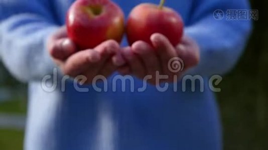 一位身材矮小的年轻女子用成熟的红苹果把手伸向照相机视频
