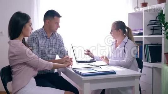 年轻的家庭医生，一位医生咨询一对夫妇坐在医疗办公室的办公桌前的生育率视频