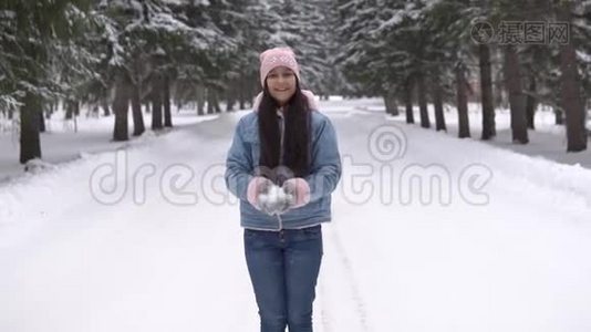 心情好的漂亮女孩站在冬天的森林里微笑着，用手吹雪。 慢动作视频