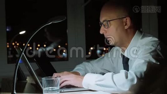 一个专注于笔记本电脑的商人，在黑暗的办公室里用电话交谈视频