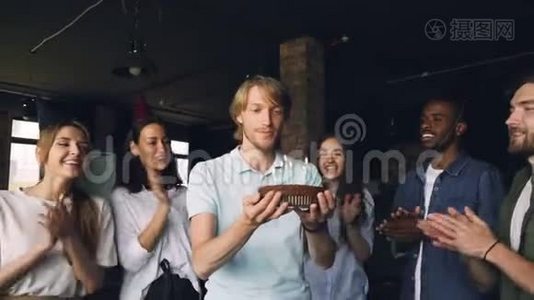 一个满脸表情的大胡子正在许愿，在生日蛋糕上吹蜡烛，而他的同事们正在鼓掌视频