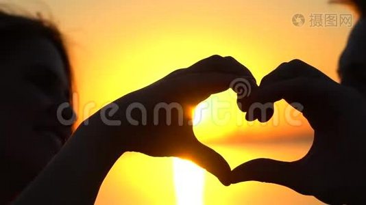 幸福的年轻夫妇在日落时用手在海洋上做心形。 日落海上的男人和女人剪影视频