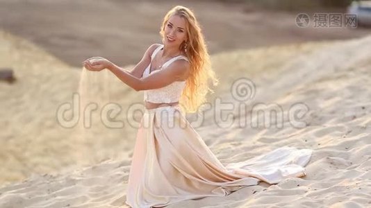 美丽新娘的肖像穿着时尚的飞行礼服，坐在迪拜大沙漠的沙滩上。视频