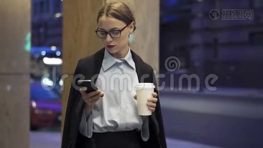 女商人带着咖啡散步和上网，她的智能手机视频
