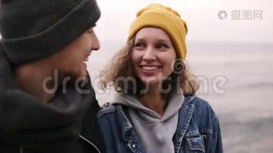 一对时髦的年轻幸福夫妇站在一起，在海边拥抱。 穿暖和衣服的年轻人视频