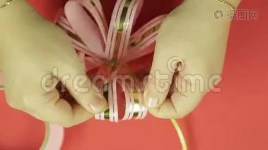 女人`双手伸直粉红色丝带礼物蝴蝶结的花瓣，给它蝴蝶结的形状。 红色背景视频