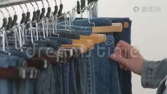 各种各样的女人`牛仔裤挂在衣架上。 女人在商店里挑选衣服。 双手合拢视频