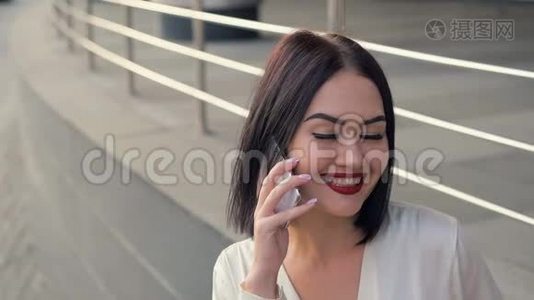 一位微笑优雅的女人的肖像，用红色口红在手机上交谈，特写户外快乐的肖像。视频