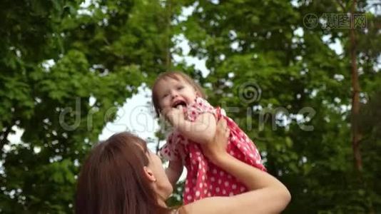 小女孩在妈妈的手里跳着，笑着。 妈妈在夏天公园和她女儿玩。 慢慢视频