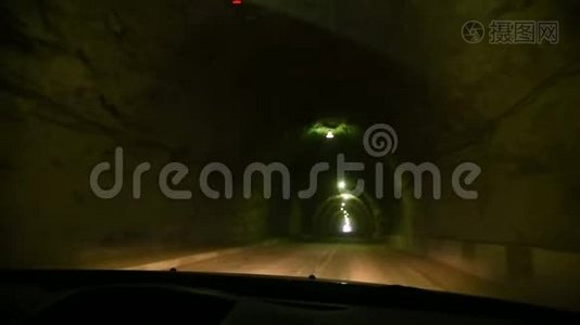 透过汽车的挡风玻璃看。这辆汽车穿过一条用昏暗的灯光和乡村的岩石建成的隧道视频
