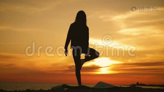 剪影年轻女子在海上日落时练习瑜伽。 快乐的生活时刻-海滩上的剪影瑜伽视频