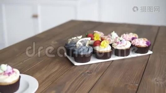 工作室厨房木桌上装饰的糕点的录像。 不同颜色的纸杯蛋糕，摩丝奶油，粉红色，蓝色视频