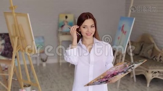 一个笑女孩画家的肖像在一个灯光工作室与调色板的颜色。视频