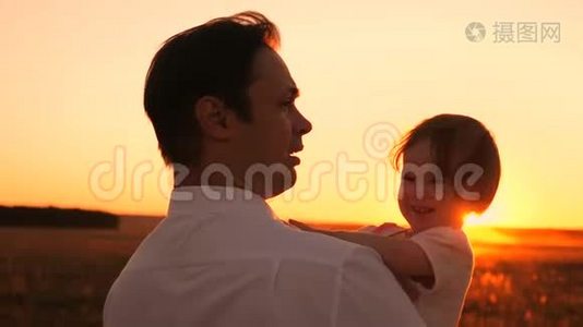 快乐的爸爸和小女儿坐在她的怀里，夕阳下，灿烂的阳光。 女孩笑着和爸爸在晚上散步视频