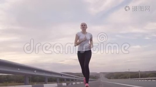 健康的生活方式。 一个穿着白色T恤和明亮运动鞋的女孩在日落时分从城市的道路上奔跑，头发视频
