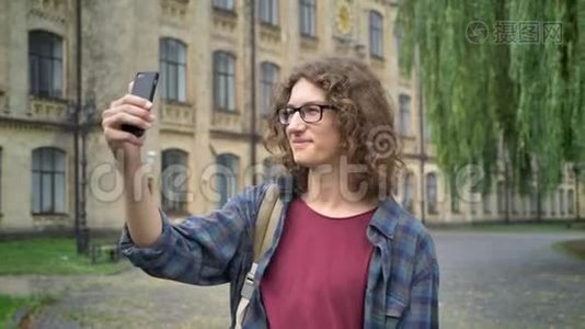 年轻帅气的学生戴着眼镜，留着长长的卷发，在大学附近的大街上进行视频聊天，站在户外视频