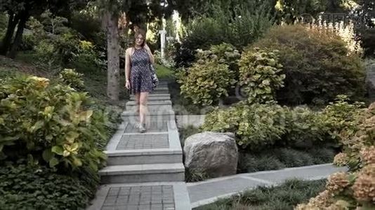 一个年轻的女孩走下美丽的台阶，这台阶位于一个有各种奇花异草和树木的绿色公园里视频