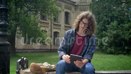 聪明认真的学生，留着平板眼镜，留着长长的卷发，坐在大学或校园附近公园的长椅上视频