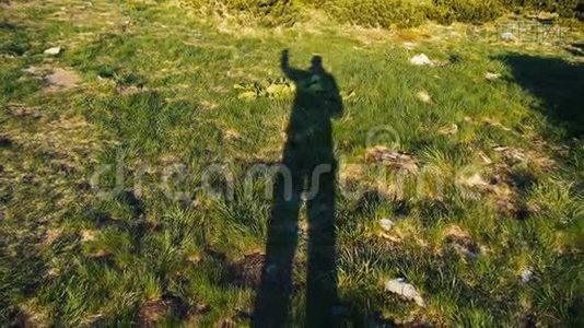 一个高大的人用手缓慢地举起绿色草坪的影子视频