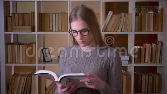年轻漂亮的女学生戴着眼镜，看着一本书，微笑着看着镜头的特写照片视频