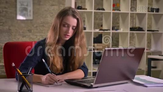 白种人金发女商人的肖像，她专心地用笔记本电脑工作，并在办公室做笔记。视频