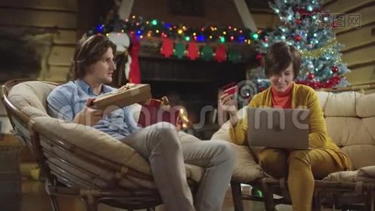 美丽的成年女子在网上买笔记本电脑，和拿着圣诞礼物的年轻人交谈视频
