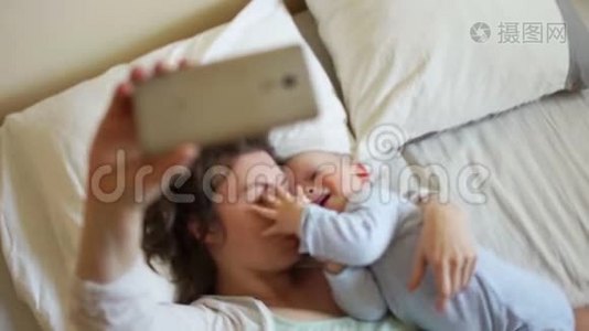 幸福的妈妈和宝宝躺在床上拍摄摄像机手机视频