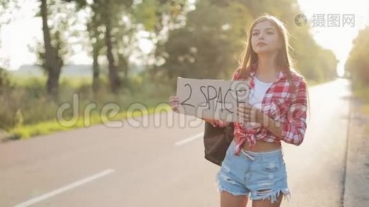 年轻美女搭便车站在路上举着2个空间标志。 夏季视频