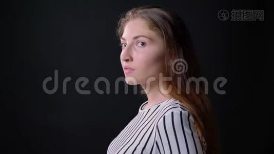 年轻焦虑的女人转过头看着摄像机，站在黑色背景上，严肃而自信视频