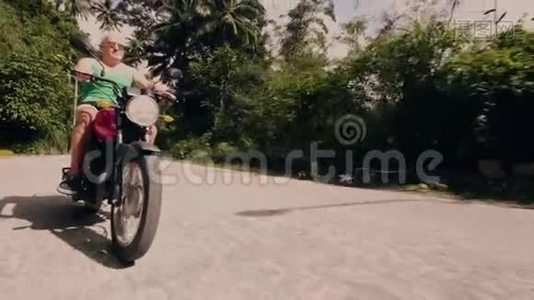 骑摩托车在热带森林景观道路上的老人。 一个骑摩托车的老人在摩托旅行视频